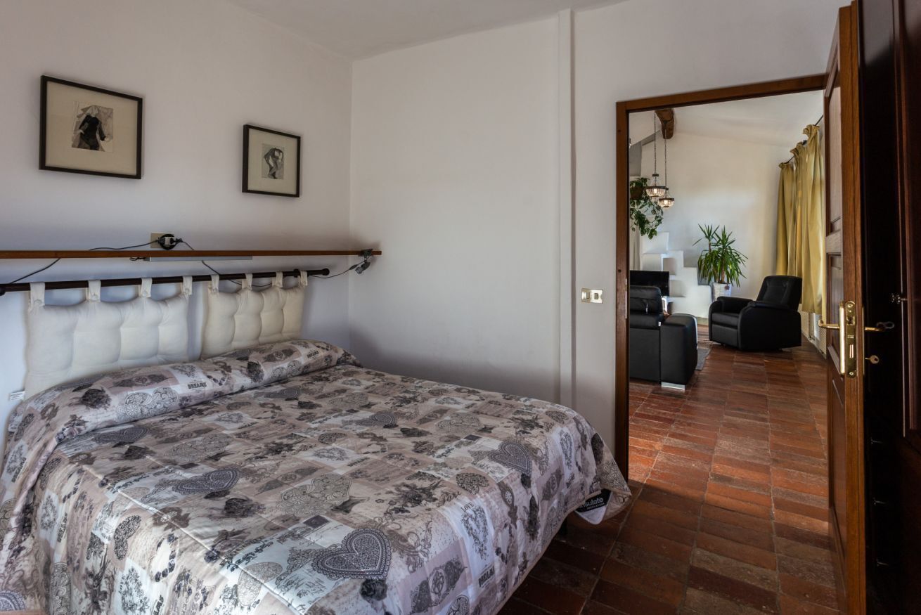 Una camera da letto con un letto, una testiera in legno e un'apertura che dà su un soggiorno con un divano e una poltrona.
