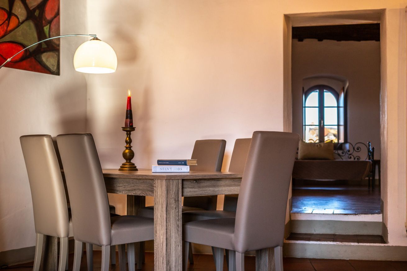 Un comedor con una mesa de madera, cuatro sillas, una vela y un libro titulado 'STEVE JOBS'.