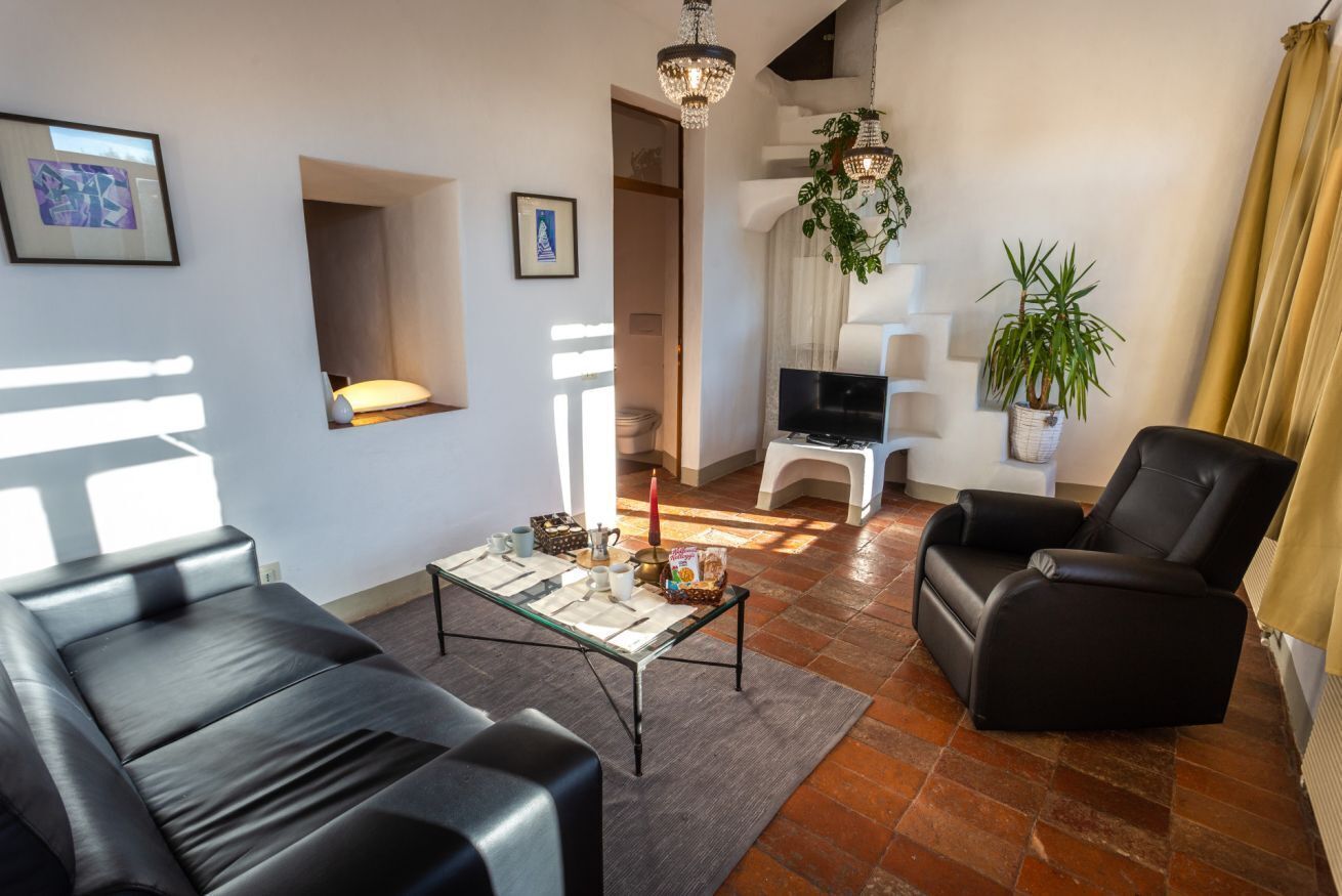 Ein modernes Wohnzimmer mit einer Couch, einem Couchtisch und einem Fernseher. Es befinden sich Pflanzen und eine Kristallleuchter dort.