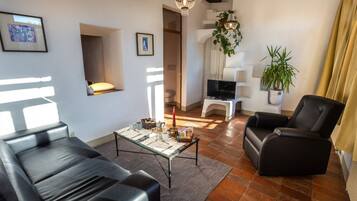 Ein modernes Wohnzimmer mit einer Couch, einem Couchtisch und einem Fernseher. Es befinden sich Pflanzen und eine Kristallleuchter dort.