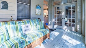 A covered porch with a striped sofa, a wooden bench, and a door leading to a room with shelves. - RESTFUL RETREAT! (Hilton Head Island)