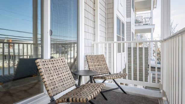 En balkong med två fåtöljer i rotting och ett litet bord, med utsikt över ett bostadsområde.