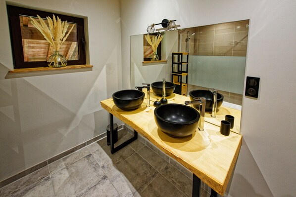 Une salle de bain moderne avec un meuble-lavabo en bois, deux vasques noires, un récipient en verre et un miroir avec un cadre en bois.