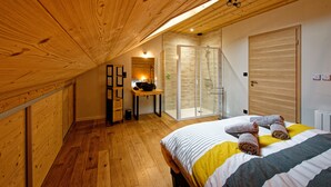 A bedroom with a wooden ceiling, a bed with rolled towels, a small table with a bowl, and a sliding glass door leading to a balcony.