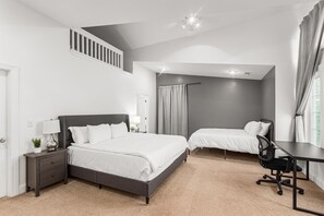 Ein Schlafzimmer mit einem großen Bett, einem Schreibtisch und einem Sessel. Es gibt ein Fenster mit Vorhängen und einen Deckenventilator.