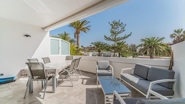Terraza en la azotea con zona de comedor, asientos y vistas a palmeras y edificios.