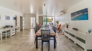 Un comedor amplio con una mesa larga y sillas, una zona de cocina con electrodomésticos modernos, y vistas al exterior.
