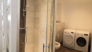 Ein kleines Badezimmer mit Dusche, Toilette und Waschmaschine.