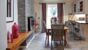 Una cocina moderna con pared de piedra, un comedor con mesa y sillas de madera, y una barra con taburetes.