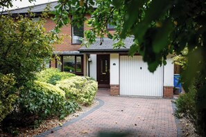 Une maison en briques avec une porte de garage blanche, entourée d’arbustes bien entretenus et d’un chemin en briques.