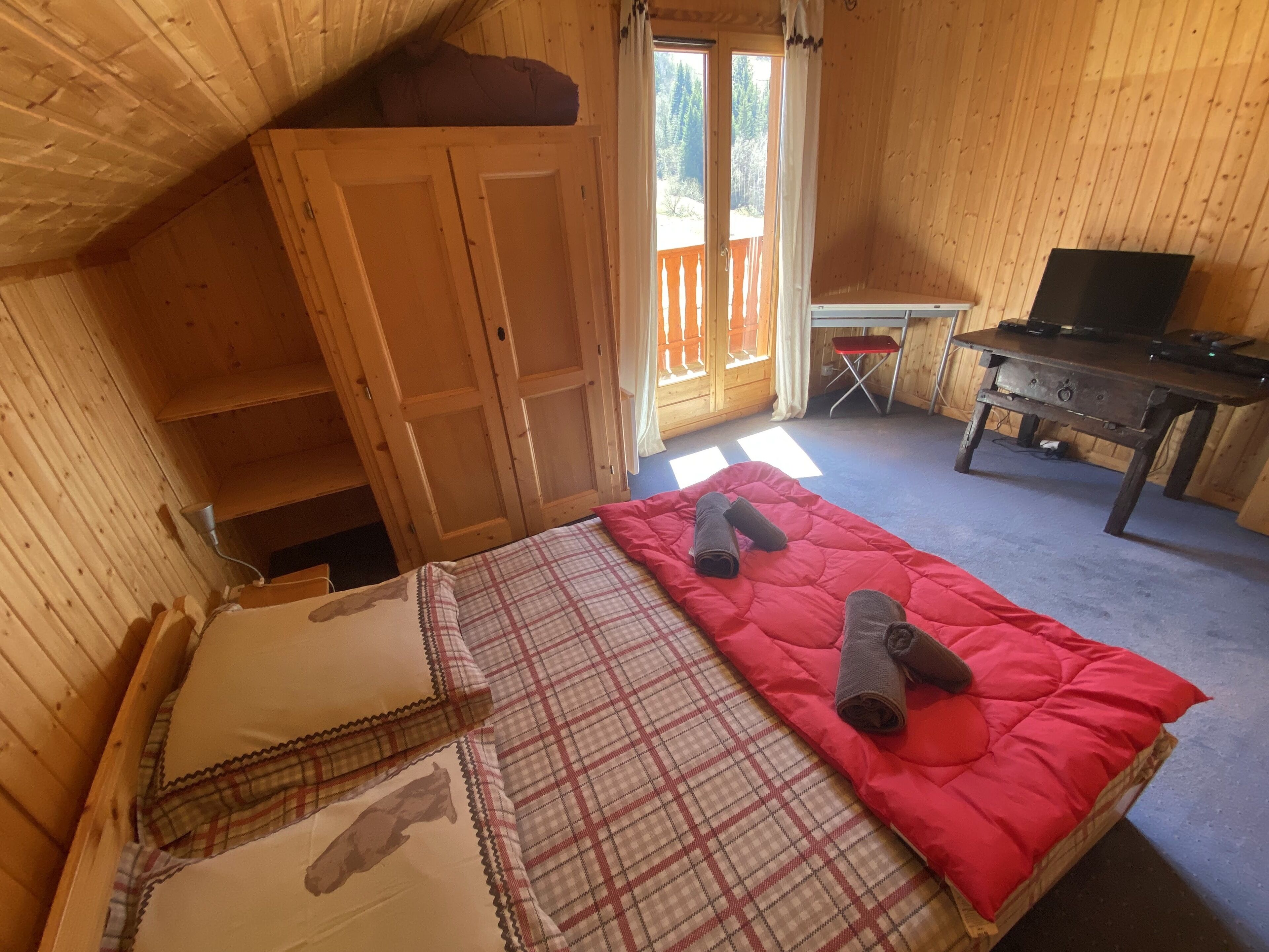 A cozy wooden room with a bed, a desk, and a television.