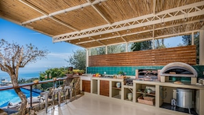 Een buitenkeuken met uitzicht op de oceaan, een zwembad en een pergola.