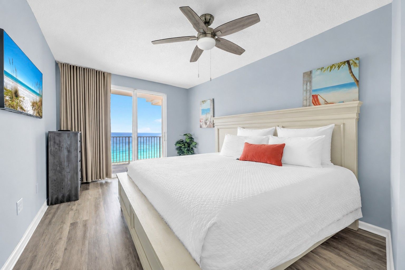 A bedroom with a bed, a ceiling fan, a view of the ocean through a window, and a balcony.