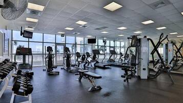 Een sportschool met diverse trainingsapparaten, grote ramen en uitzicht op buiten.