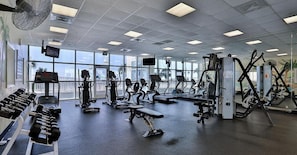 Un gimnasio con diversos equipos de ejercicio, ventanas amplias y vistas al exterior.