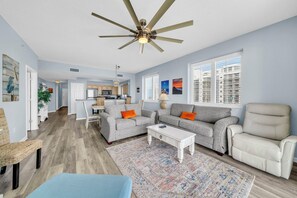 A spacious living room with a ceiling fan, a grey sofa set, a white armchair, and a patterned rug.
