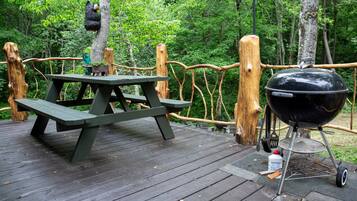 Una terraza de madera con una mesa de picnic y una parrilla portátil.