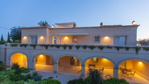 A modern villa with a covered patio, multiple arches, and a well-lit interior. - Villa Passo degli Aironi 12, Emma Villas (Noto)