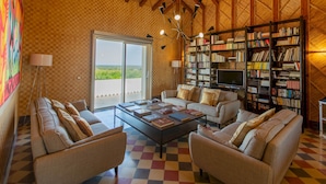 Ein geräumiges Wohnzimmer mit einem Schachbrettmuster-Boden, zwei Sofas, einem Couchtisch mit Büchern, einem Bücherregal und einem Fernseher.