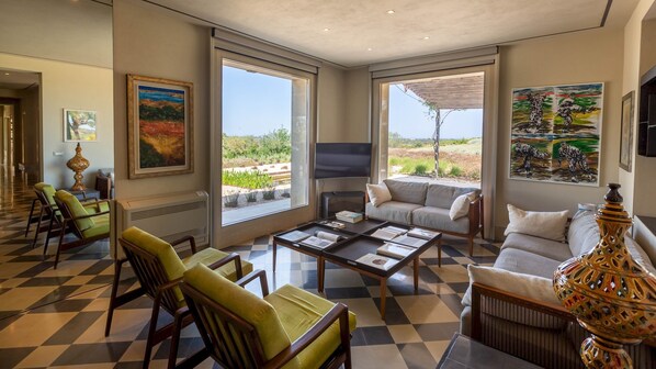 A spacious living room with a large window, a sofa, a coffee table, and a decorative lamp. - Villa Majoli 9, Emma Villas (Noto)