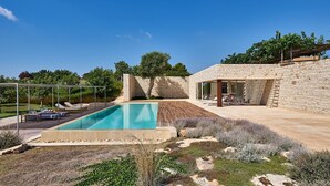 A modern outdoor pool area with a stone wall and lounge chairs. - Villa Majoli 9, Emma Villas (Noto)
