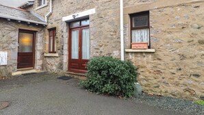 A stone building with a wooden door, a window with a curtain, and a small potted plant. - Coach House Cottage (Carnforth)