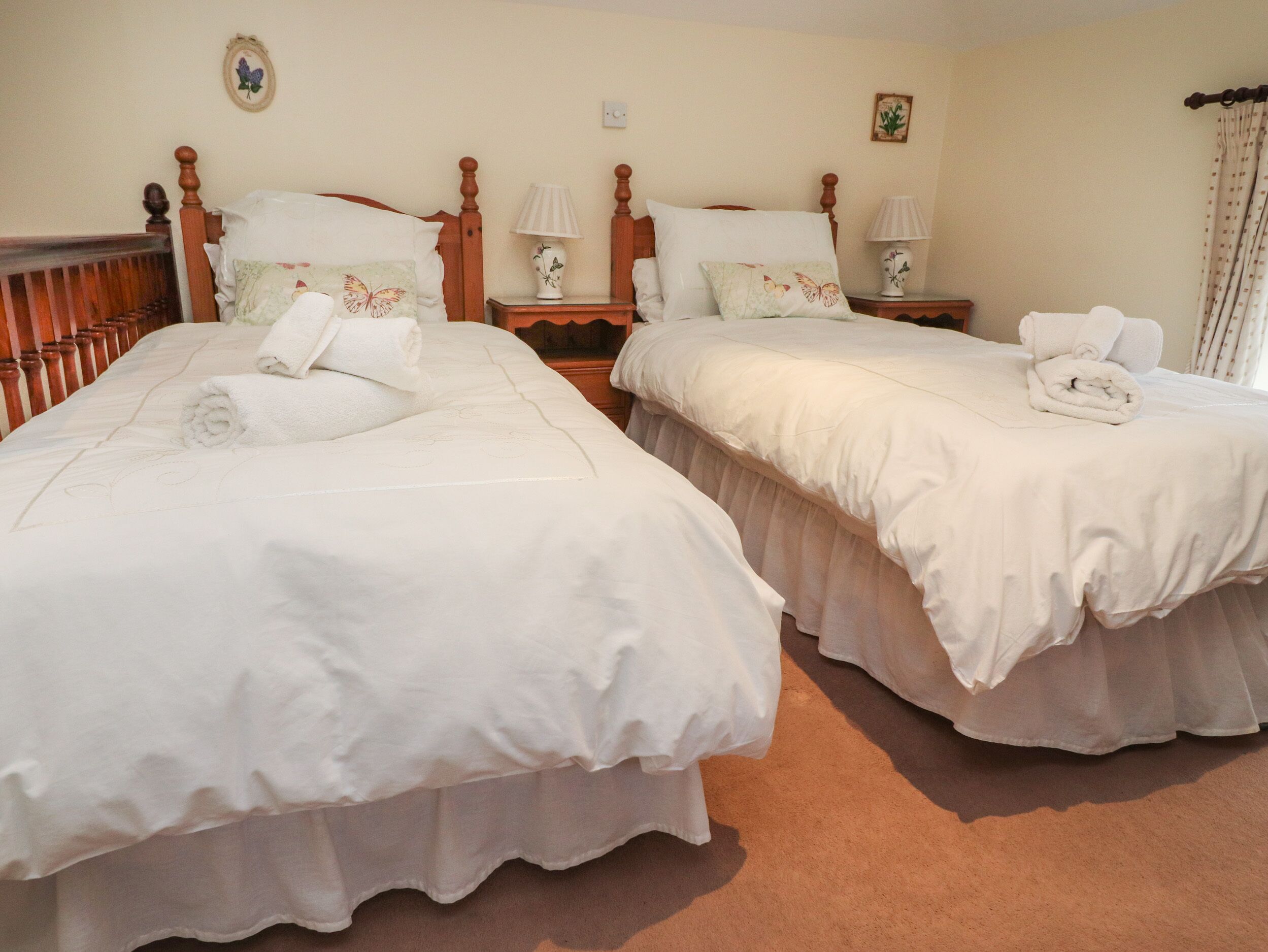 Une chambre d’hôtel avec deux lits, chacun recouvert d’une courtepointe blanche et doté d’oreillers, d’une tête de lit en bois et d’une table de chevet avec une lampe.