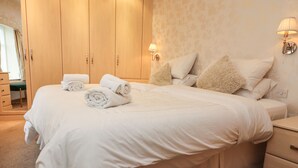 A neatly made bed with rolled towels, a wooden wardrobe, and two wall-mounted lamps. - Coach House Cottage (Carnforth)