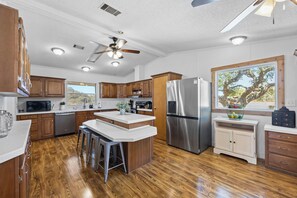 A modern kitchen with wooden cabinets, stainless steel appliances, and a central island with stools. - Flying B Ranch House on 52 acres in Bertram, TX (Burnet County)