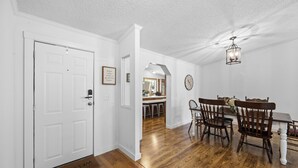 A hallway leading to a dining area with wooden flooring, a white door, and a dining table with chairs.