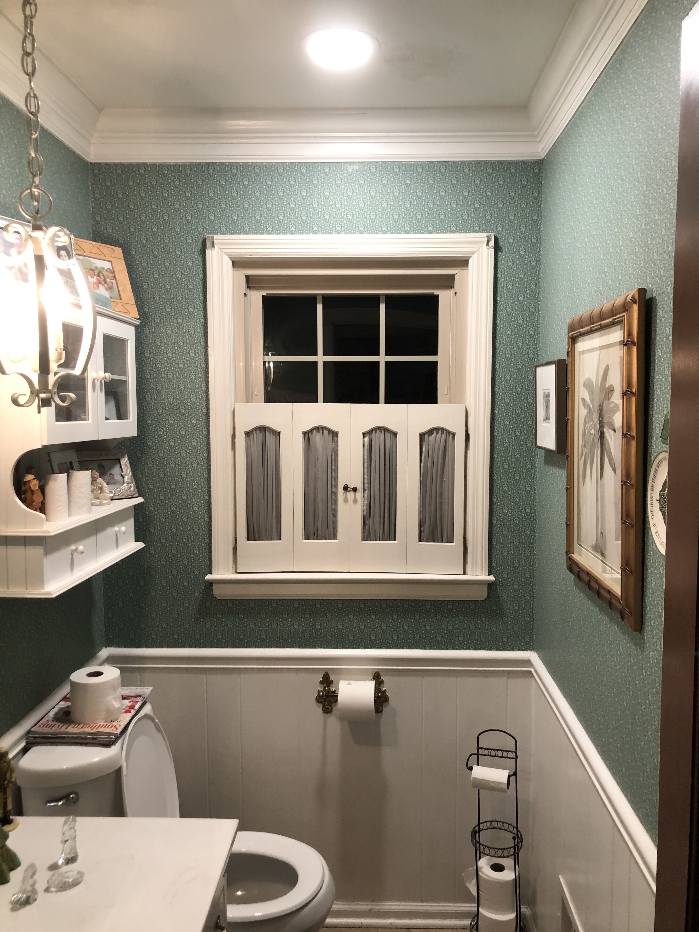 A bathroom with a toilet, sink, and window with curtains.