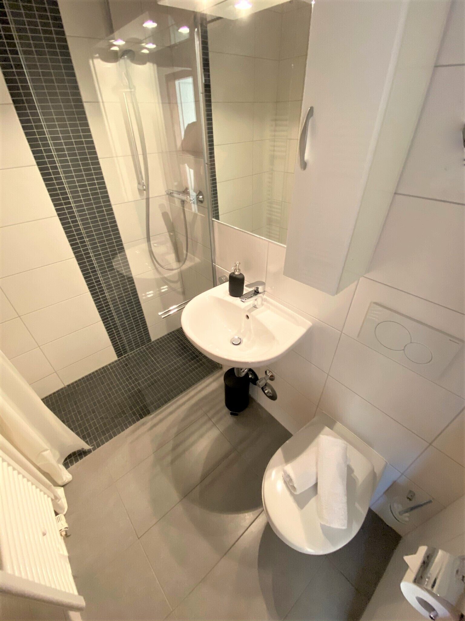 Een moderne badkamer met een douchecabine van glas, een witte wastafel en een toilet.