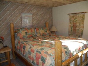 A bedroom with a wooden bed frame, a quilt, a lamp, and a tapestry on the wall.