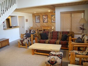 A spacious living room with a wooden staircase, a sofa set, and a dining table.
