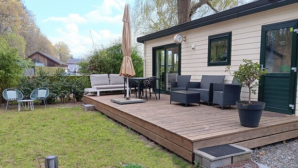 A wooden deck with outdoor furniture, a potted plant, and a small garden area with plants and a decorative metal piece.