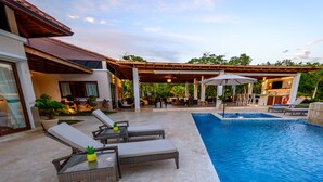 Uma área à beira da piscina com espreguiçadeiras, um bar e um espaço coberto para sentar.