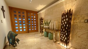 Um corredor com porta de madeira, uma escultura decorativa de peixe, uma planta e um ponto de luz fixado na parede.