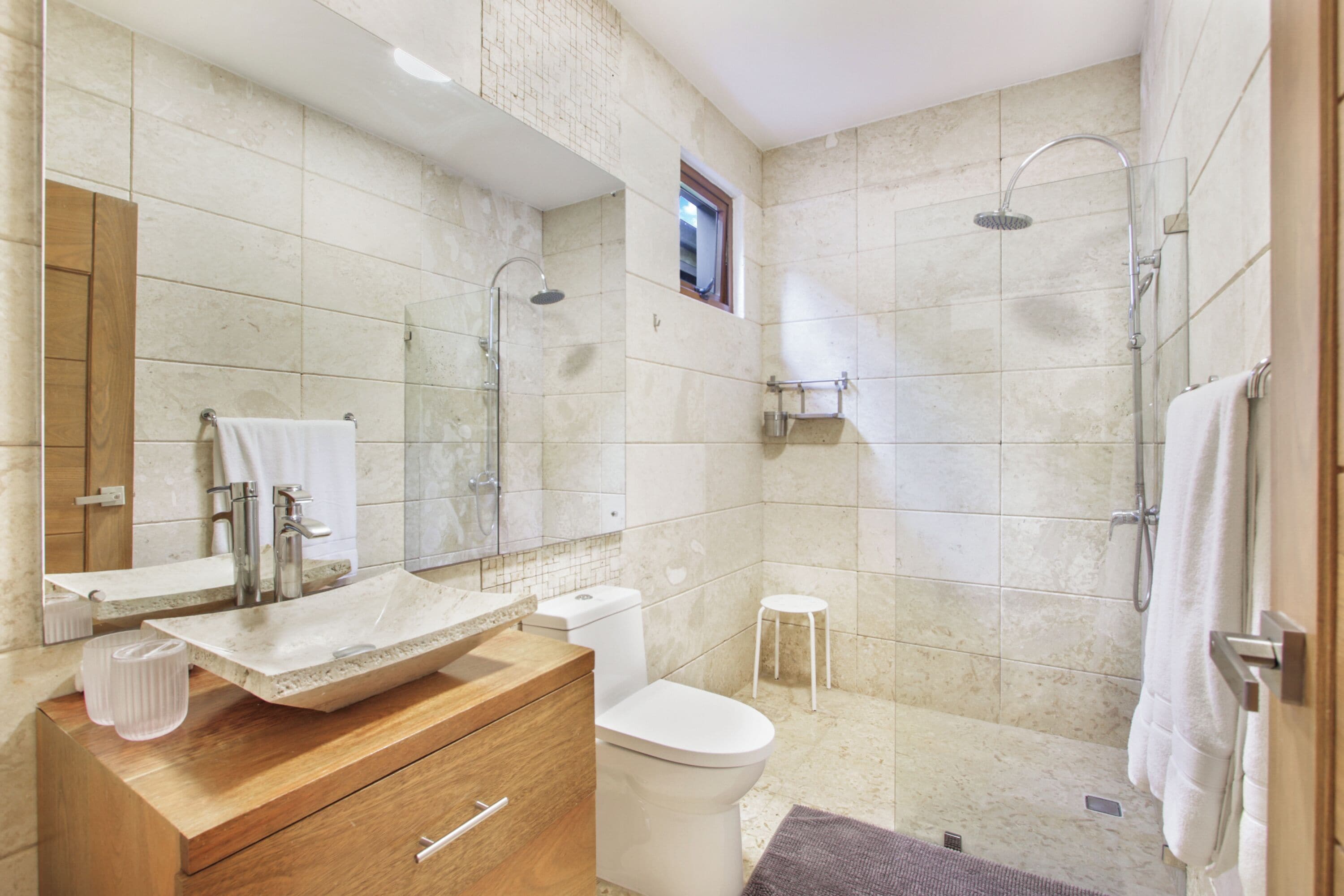 A modern bathroom with a wooden vanity, a large mirror, a white sink, and a shower area.