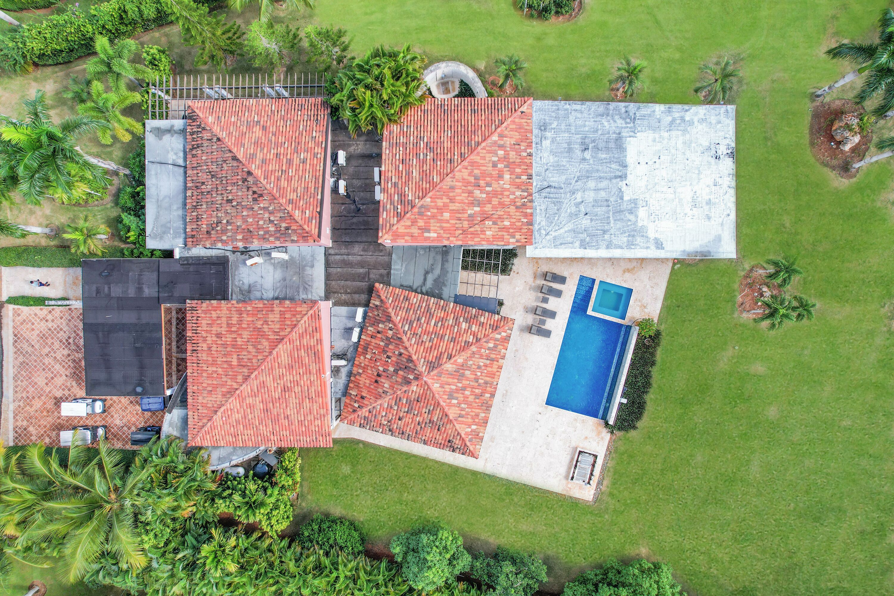Un toit-terrasse divisé en quatre sections recouvertes de tuiles rouges, une piscine et une végétation luxuriante tout autour.