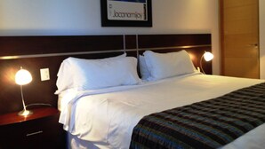 Une chambre d’hôtel avec un lit soigneusement fait, deux lampes de chevet, une table de chevet et un tableau encadré au mur.