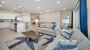 Un salon moderne comprenant un canapé, une table basse et un coin cuisine avec des meubles blancs et un réfrigérateur.
