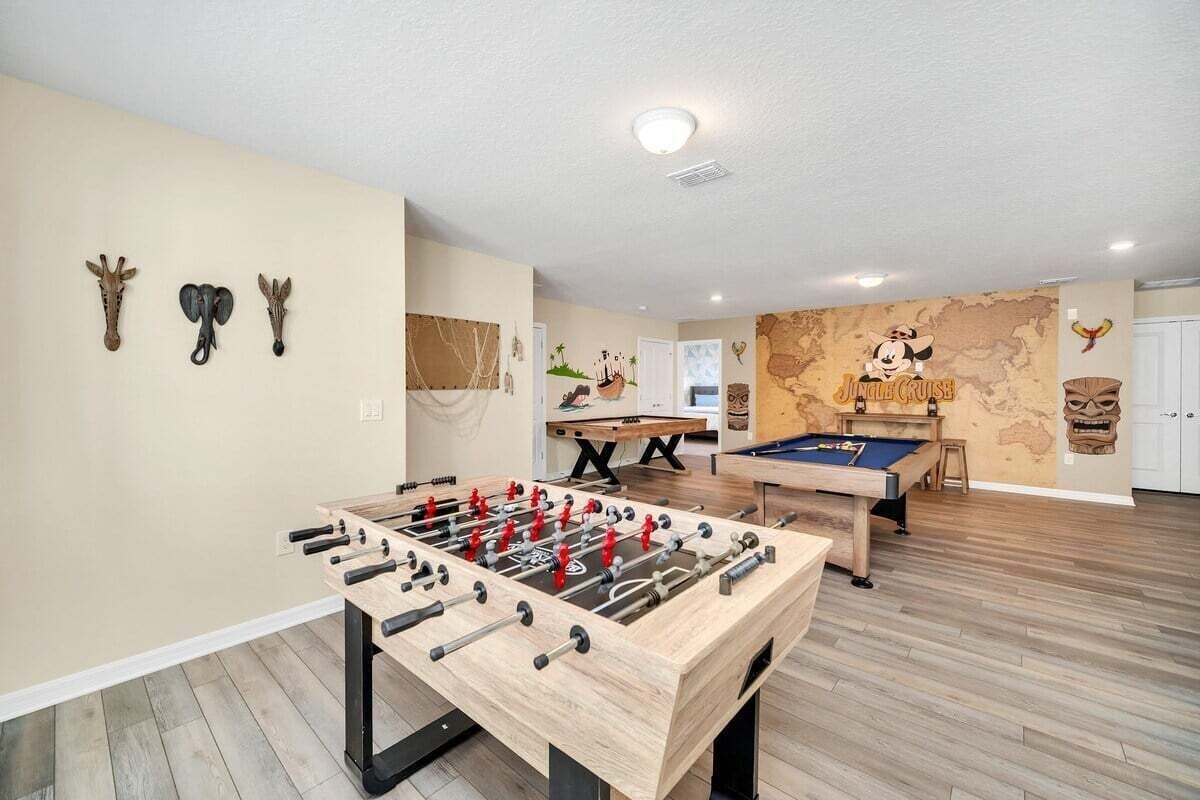 A room with a foosball table, pool table, and a wall with a map and cartoon characters.