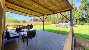 An outdoor patio with a wooden deck, a covered seating area, and a view of a backyard with a wooden fence and trees. - House garden swimming pool play in the country (Camélas)