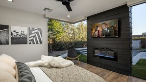 Ein modernes Schlafzimmer mit einem Bett, einem an einer dunklen Wand montierten Fernseher und einem Deckenventilator.