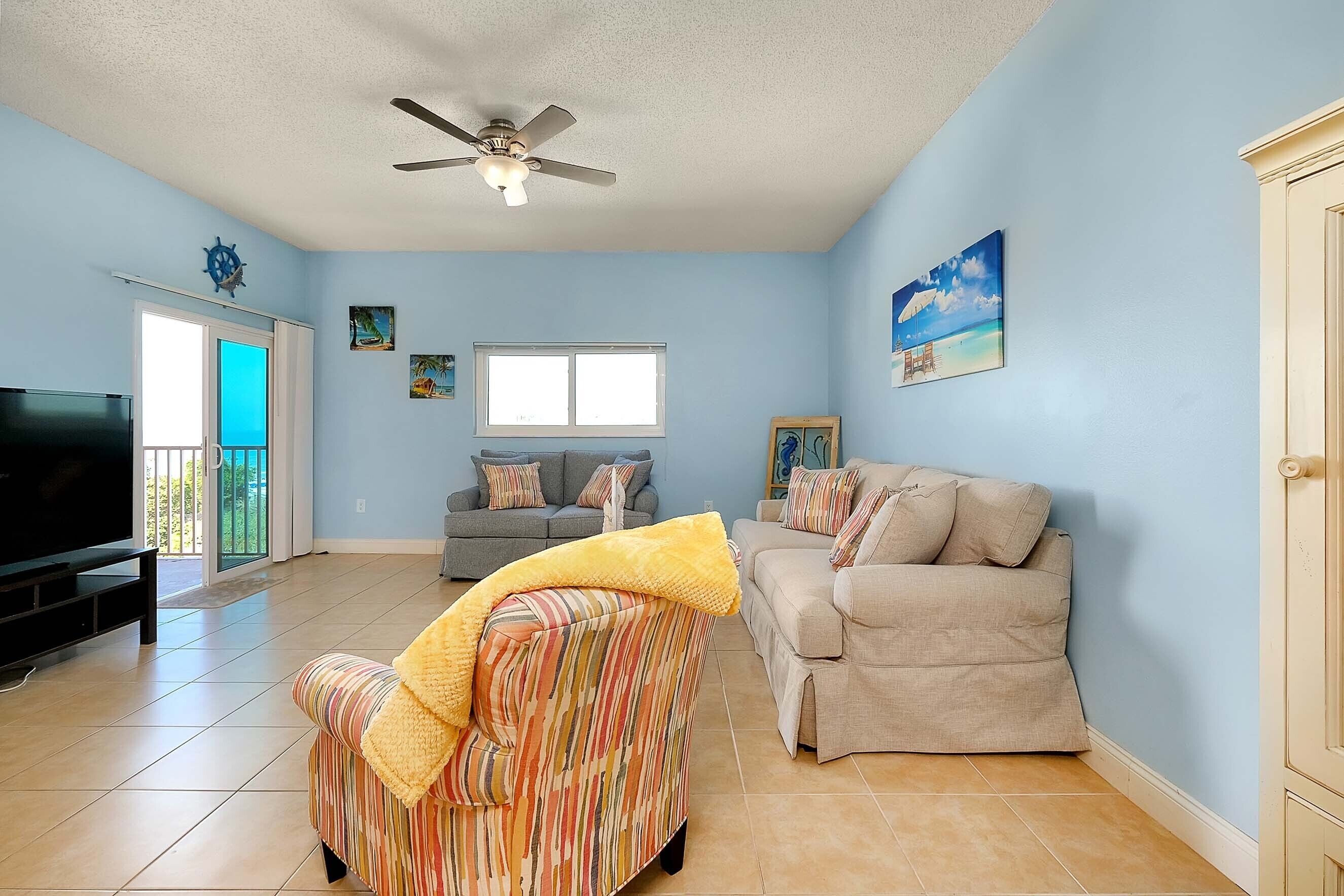 Una sala de estar con ventilador de techo, televisor, sofá y un sillón.