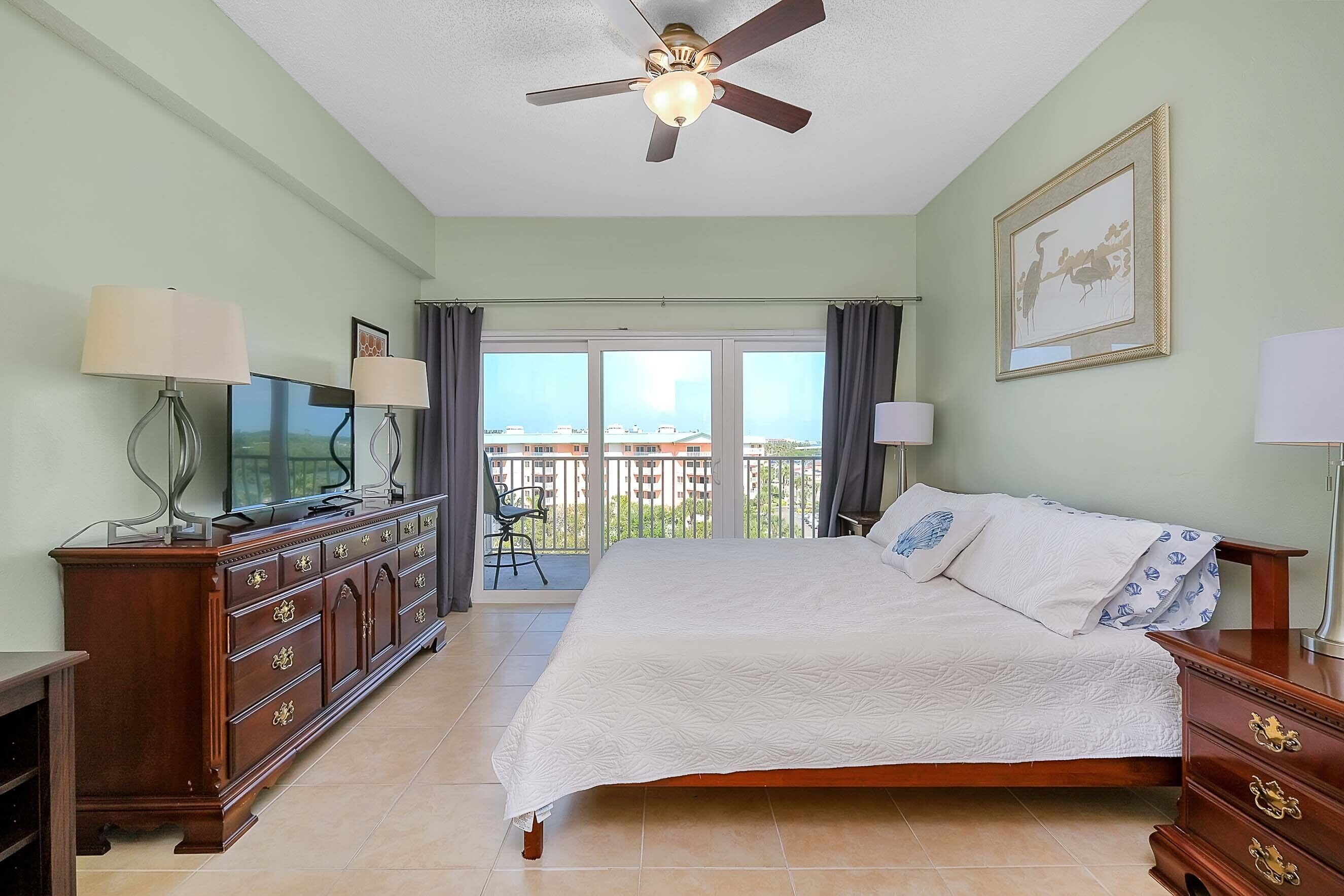 A hotel room with a bed, a TV, a dresser, and a balcony with a view.