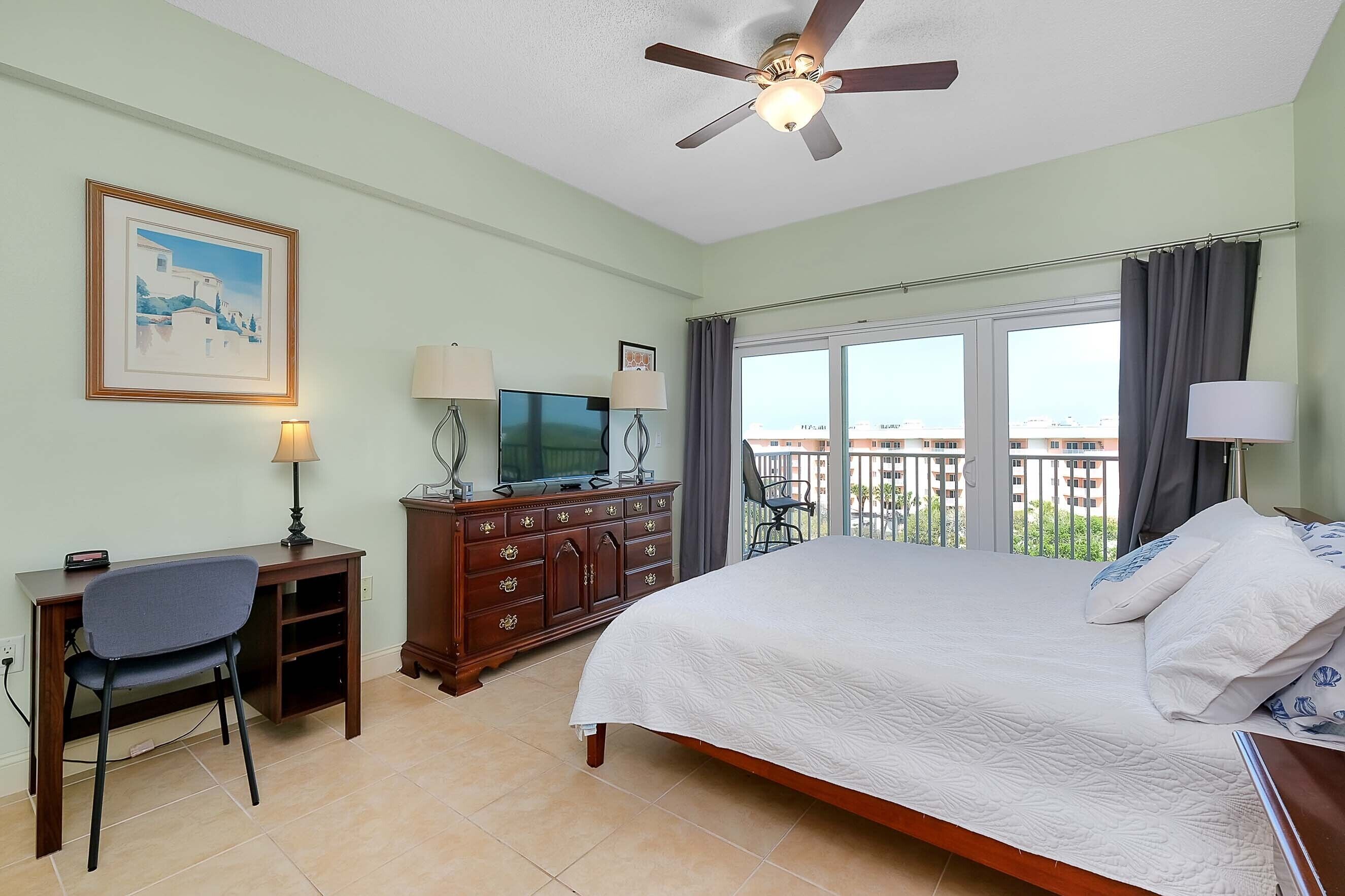A hotel room with a bed, desk, chair, TV, dresser, and a balcony with a view.