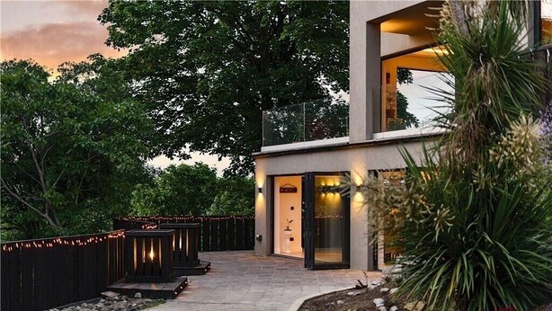 Un bâtiment moderne avec une entrée en verre, entouré d’un jardin agrémenté d’un sentier et d’un éclairage décoratif.