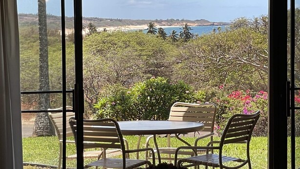A patio with a table and chairs, overlooking a scenic landscape with trees and a beach. - "Front Row"  Ocean & Island Views 2 Bedroom (Maunaloa)
