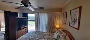 Una habitación de hotel con cama, ventilador de techo, televisor, lámpara y ventana con cortinas.